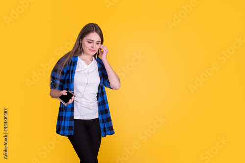 Beautiful fascinating girl in a blue shirt listening music on a yellow background