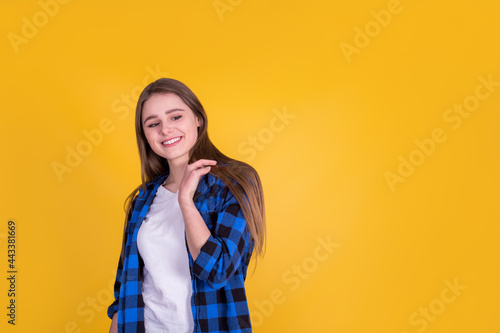 Beautiful girl with cute smile in a blue shirt on a yellow background