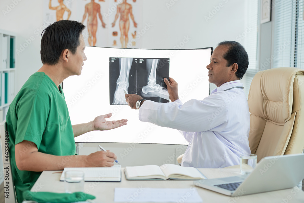 Obraz premium Serious physician discussing tumor on feet of patient when looking at x-ray image