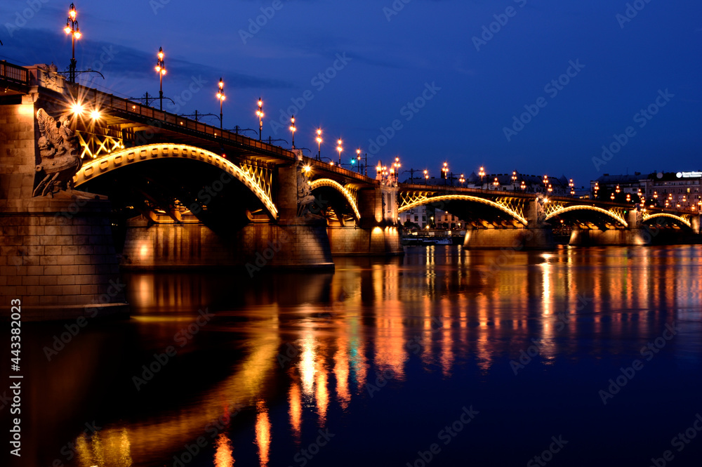 the Margaret bridge in Budapest at dusk. perspective side view. brightly illuminated steel arches. reflection on the water. tourism and travel concept. transportation and structural design. 