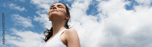 Photography low angle view of young happy woman in crop top against blue sky with clouds, ba