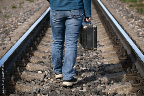 Woman with an old suitcase in her hand walks on sleepers of a railroad between rails