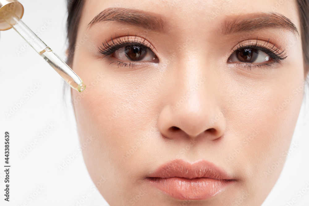 Close-up image of young woman applying hydrating face oil with vitamin C