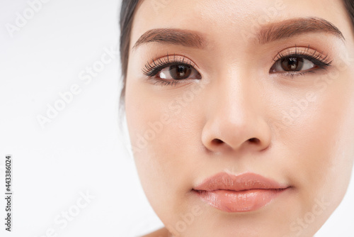 Close-up image of serious young woman with nude make-up and false lashes looking at camera