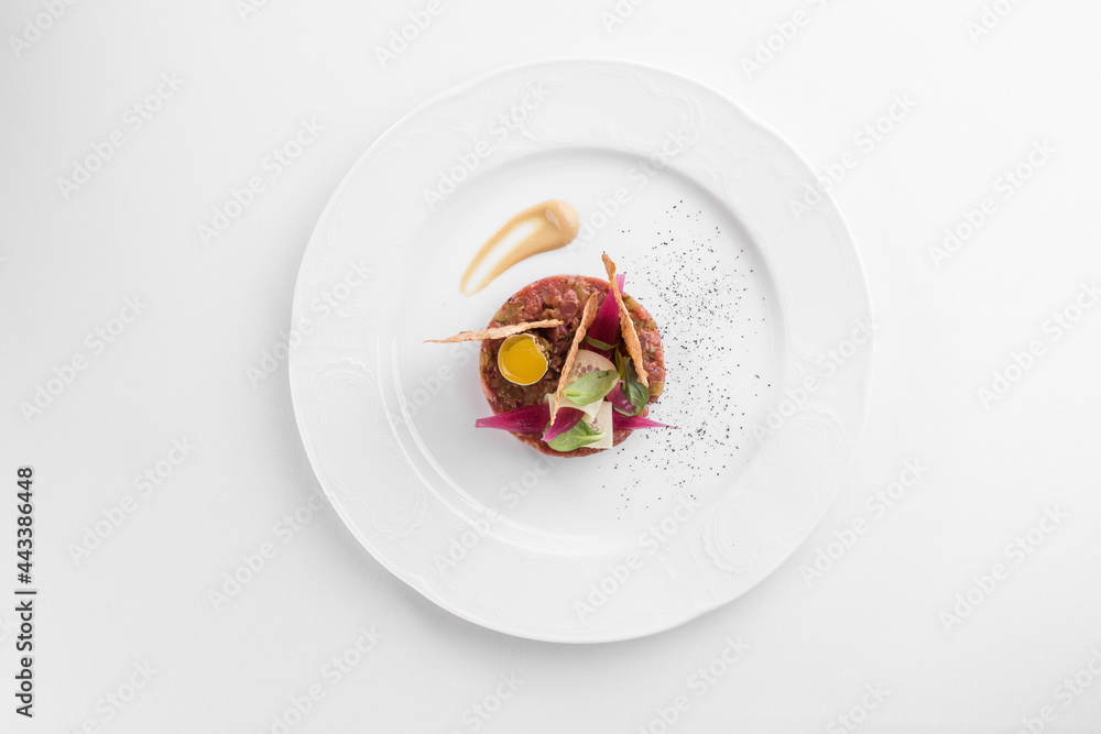 Steak tartare with yolk on white plate with onions, cucumber and bread isolated on white background Steak tartare with yolk on white plate with onions, cucumber and bread isolated on white background