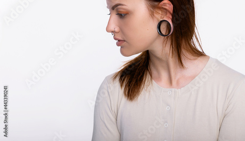 Portrait of a woman with a tunnel in her ears, and a pierced nose. White background, copy space. Woman face piercing space for text