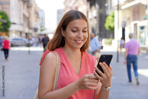 Beautiful smiling woman using smartphone in city street
