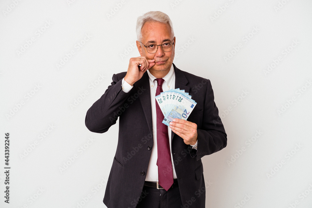Senior american business man holding bills isolated on white background with fingers on lips keeping a secret. Senior american business man holding bills isolated on white background with fingers on lips keeping a secret.