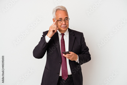Senior business american man holding mobile phone isolated on white background pointing temple with finger, thinking, focused on a task. © Asier