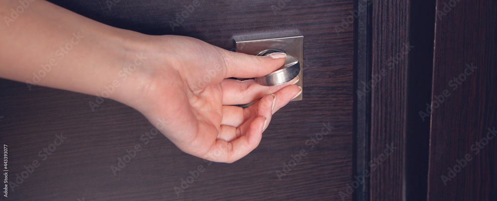 Naklejka premium Female hand on metal door handle. Modern interior detail