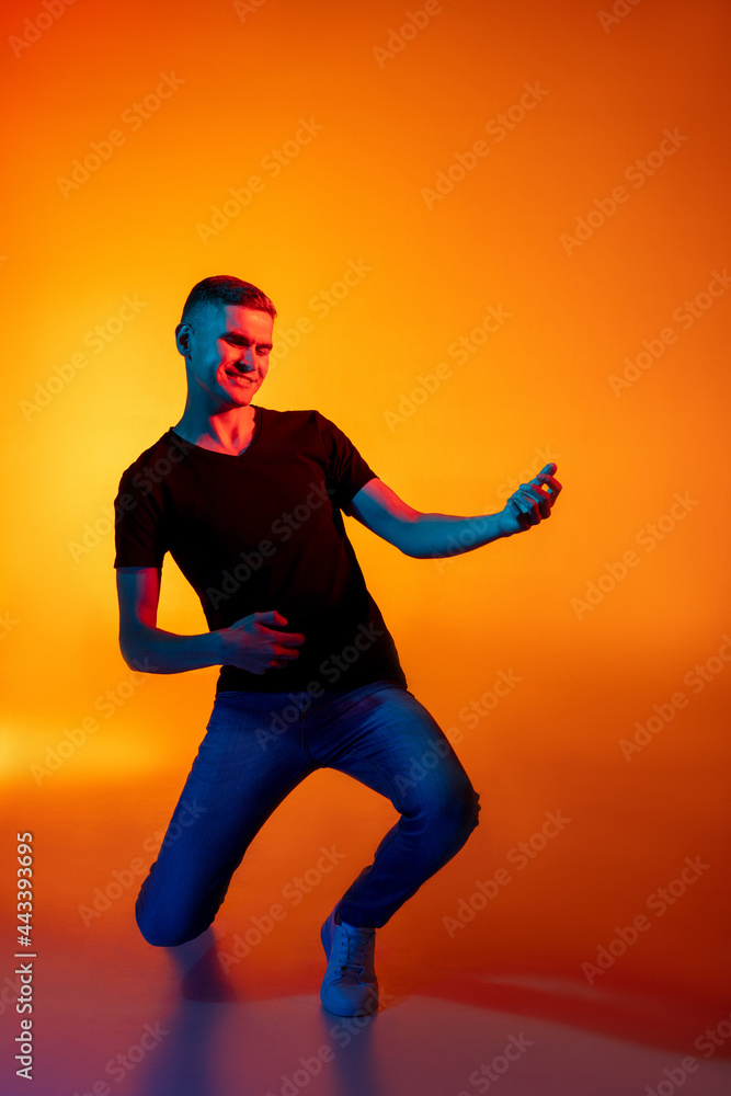 Portrait of young Caucasian man in casual clothes isolated over gradient red orange studio background in neon light with copyspace for ad. Concept of human emotions