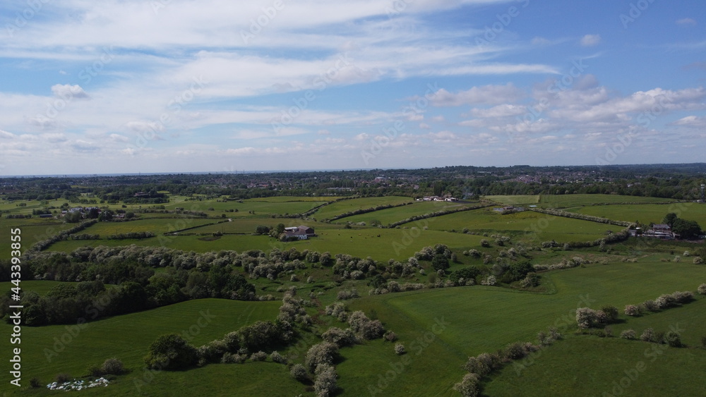 Aerial view over green farmland with a cloudy sky background. 