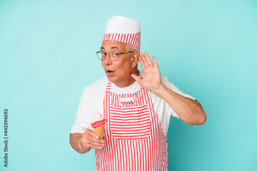 Senior american ice cream maker holding an ice cream isolated on blue background trying to listening a gossip. Senior american ice cream maker holding an ice cream isolated on blue background trying to listening a gossip.