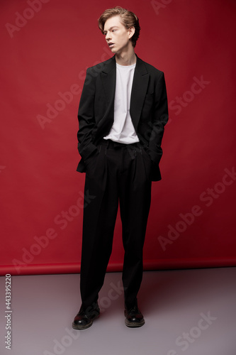 Young guy in a casual suit and white T-shirt on a red background looks to the side