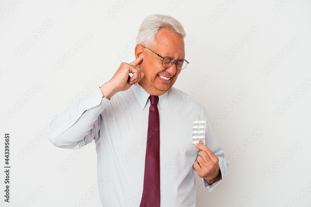 Senior american man holding pills isolated on white background covering ears with hands. Senior american man holding pills isolated on white background covering ears with hands.