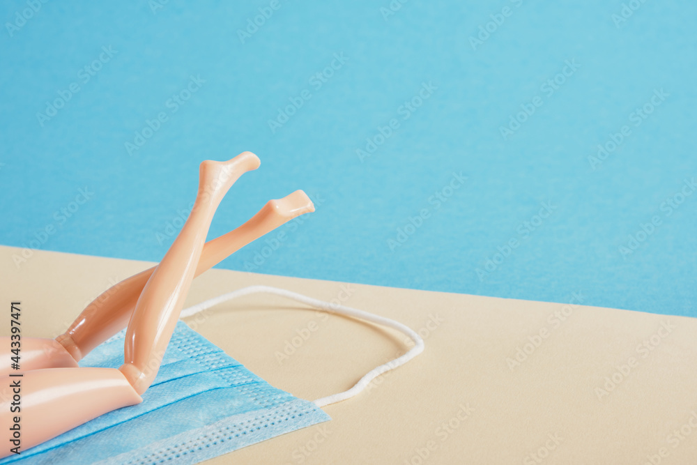 doll's legs lie on a blue face mask on a blue and beige background, beach vacation and tuzism