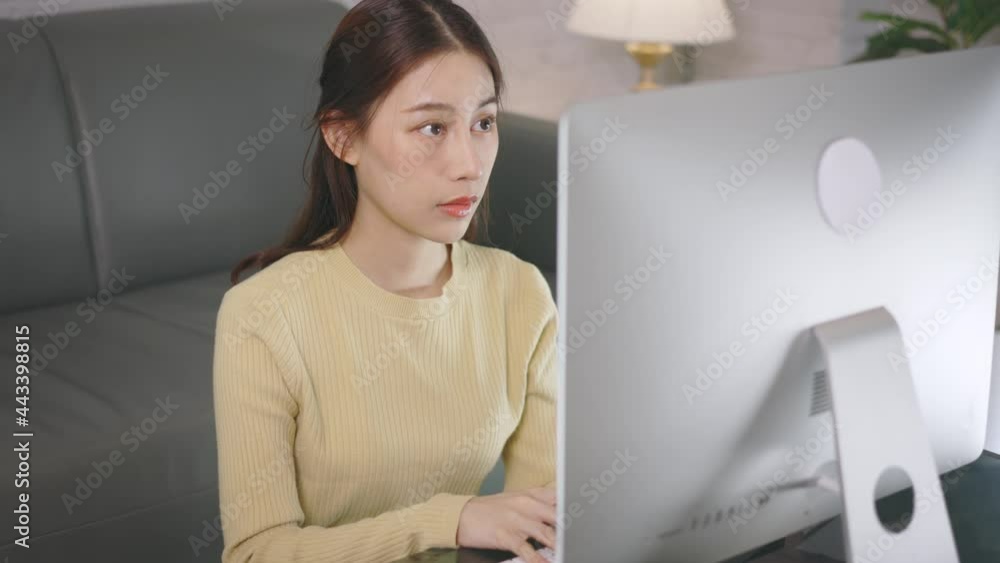 Young Asian businesswoman working from home and typing on keyboard using desktop computer while sitting in living room. Young Asian businesswoman working from home and typing on keyboard using desktop computer while sitting in living room.