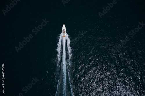 Speedboat movement on the water.Speedboat wave speed water. Large white boat driving on dark water. Speedboat on dark blue water aerial view. Speed boat faster movement on the water top view. © Berg