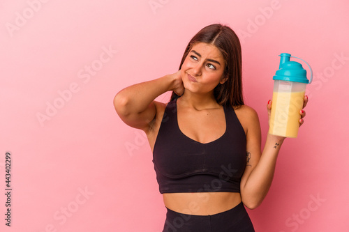 Young caucasian woman holding a protein shake isolated on yellow background touching back of head  thinking and making a choice.