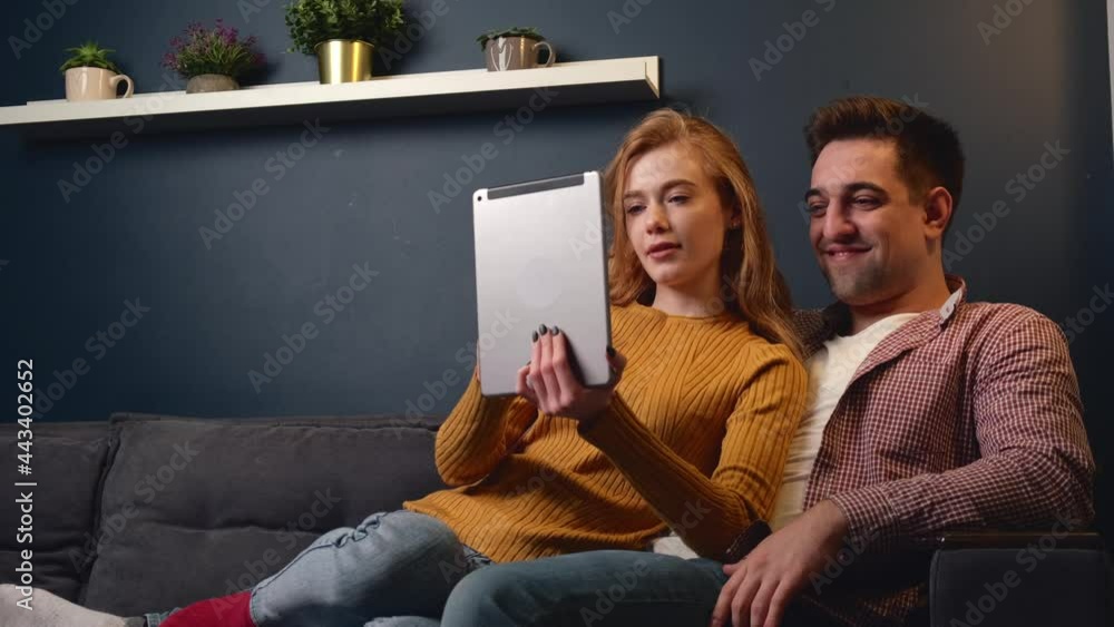 Lovely ginger woman with freckles and her lover using a tablet while lying on a sofa at home Lovely ginger woman with freckles and her lover using a tablet while lying on a sofa at home