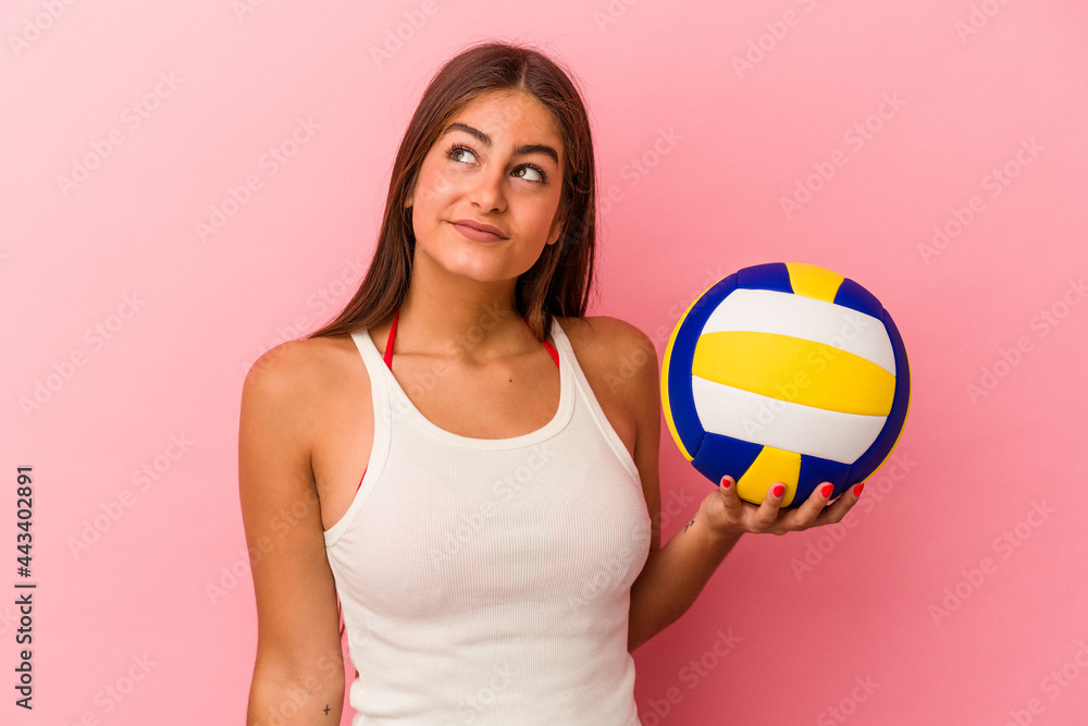 Young caucasian woman holding a volleyball ball isolated on pink background dreaming of achieving goals and purposes