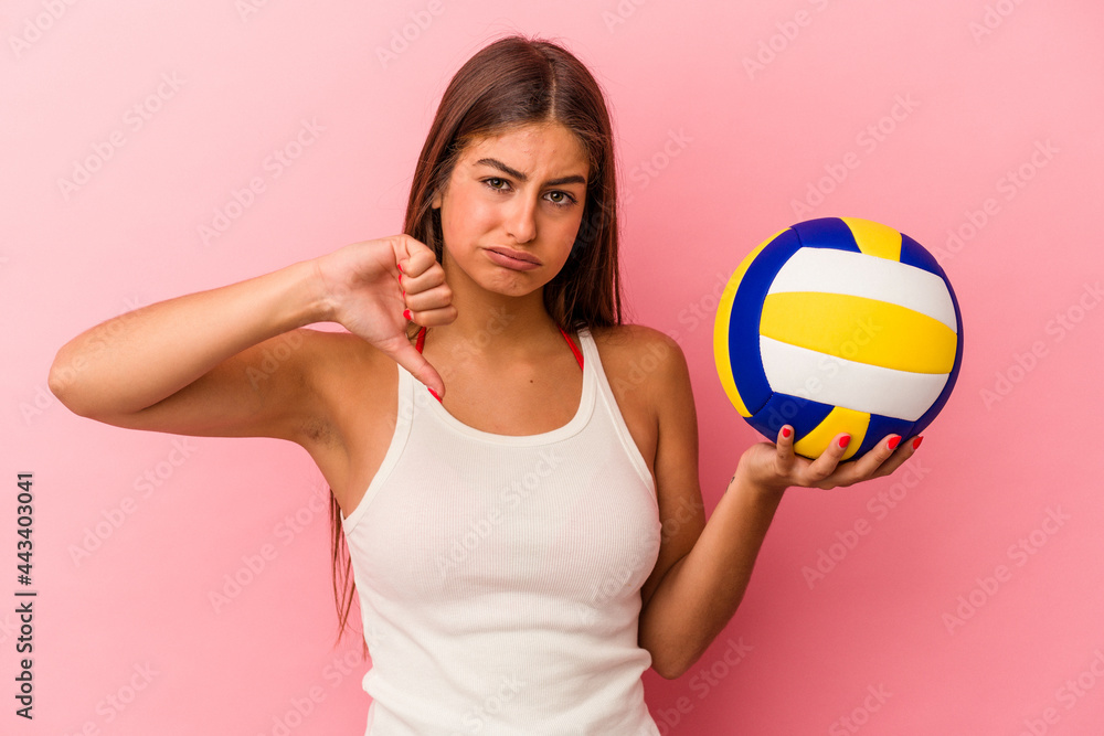 Young caucasian woman holding a volleyball ball isolated on pink background showing a dislike gesture, thumbs down. Disagreement concept.