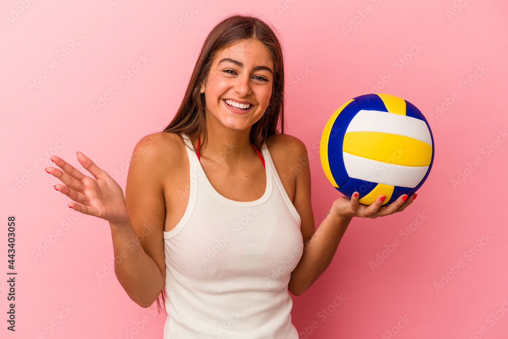Young caucasian woman holding a volleyball ball isolated on pink background receiving a pleasant surprise, excited and raising hands.