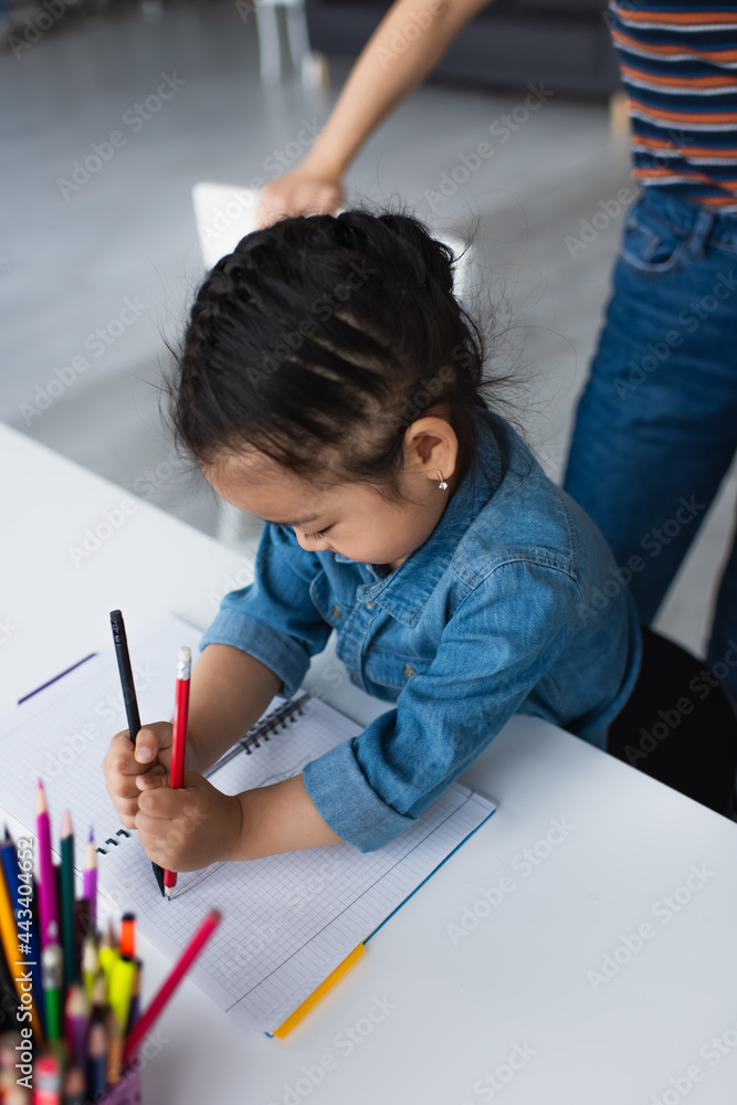 Asian girl drawing near blurred color pencils and parent at home Asian girl drawing near blurred color pencils and parent at home
