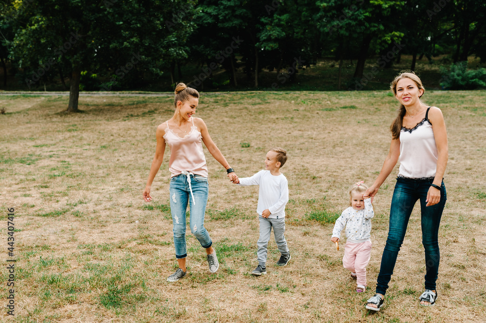 Obraz premium Two mothers with kids walking on nature on summer day. Mom and son, daughter walk in the park. Concept of happy family. Close Up.