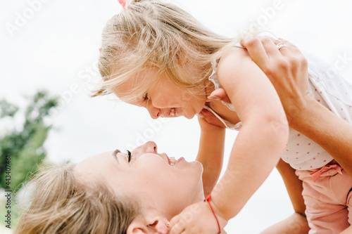 Portrait of a mother holds, throws up and spins the daughter on hands on nature on summer day. Mom and girl playing in the park. Concept of friendly family. Close Up.
