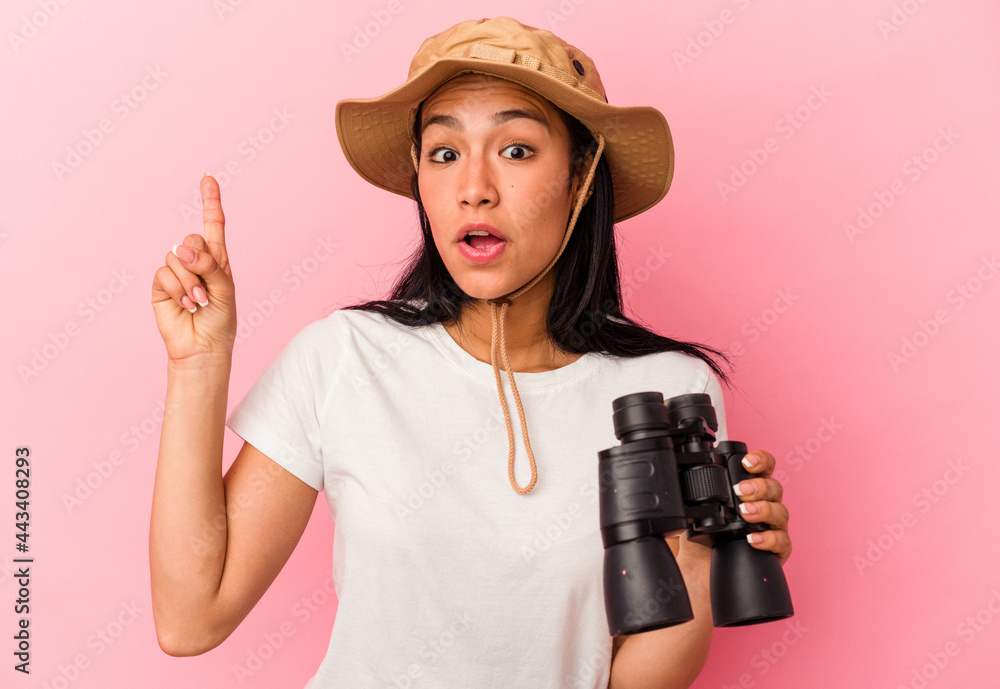Young mixed race explorer woman holding binoculars isolated on pink background having an idea, inspiration concept. Young mixed race explorer woman holding binoculars isolated on pink background having an idea, inspiration concept.