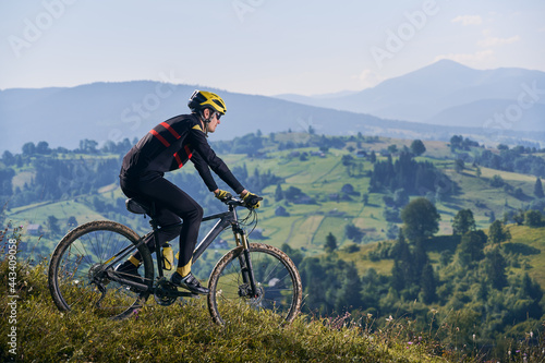 Horizontal snapshot of man riding his bike in the mountains in early foggy morning going downhill. Peaks in clouds, green hills on background. Side view, copy space. Concept of active lifestyle