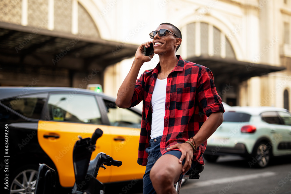 Portrait of handsome african man using electric bike in the city. Happy young man using the phone.