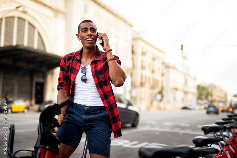 Portrait of handsome african man using electric bike in the city. Happy young man using the phone.