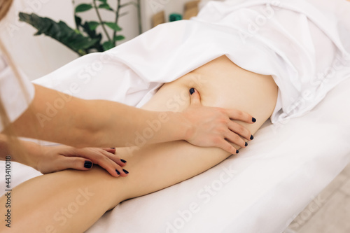 Professional is massaging and touching skin of female client, using traditional techniques. Specialist works with body of patient. Masseur is doing massage of back of woman lying in beauty salon