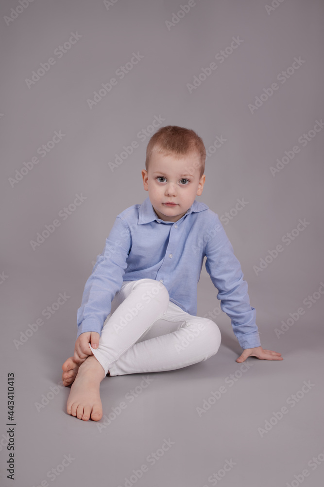 preschool blonde boy in white pants and blue shirt on grey background. child, kid isolated preschool blonde boy in white pants and blue shirt on grey background. child, kid isolated