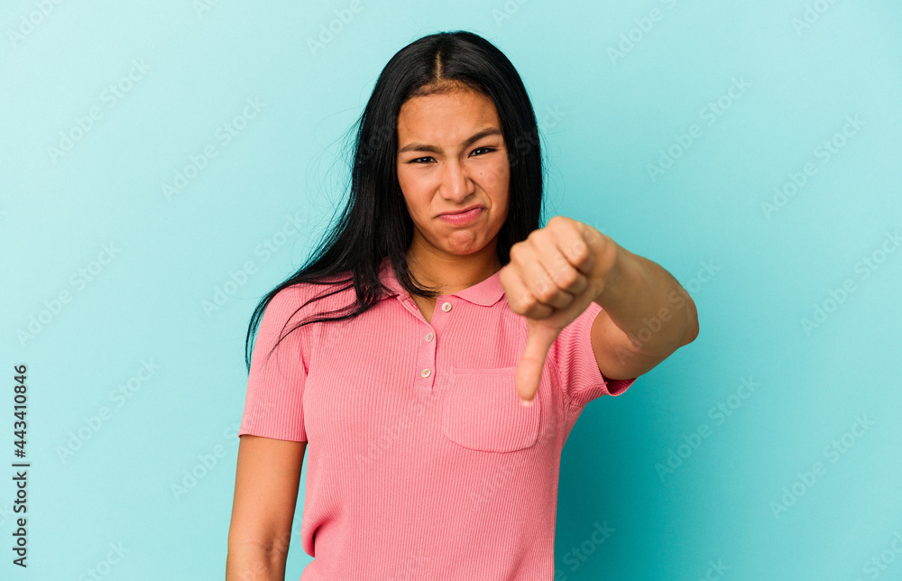 Young Venezuelan woman isolated on blue background showing thumb down and expressing dislike. Young Venezuelan woman isolated on blue background showing thumb down and expressing dislike.