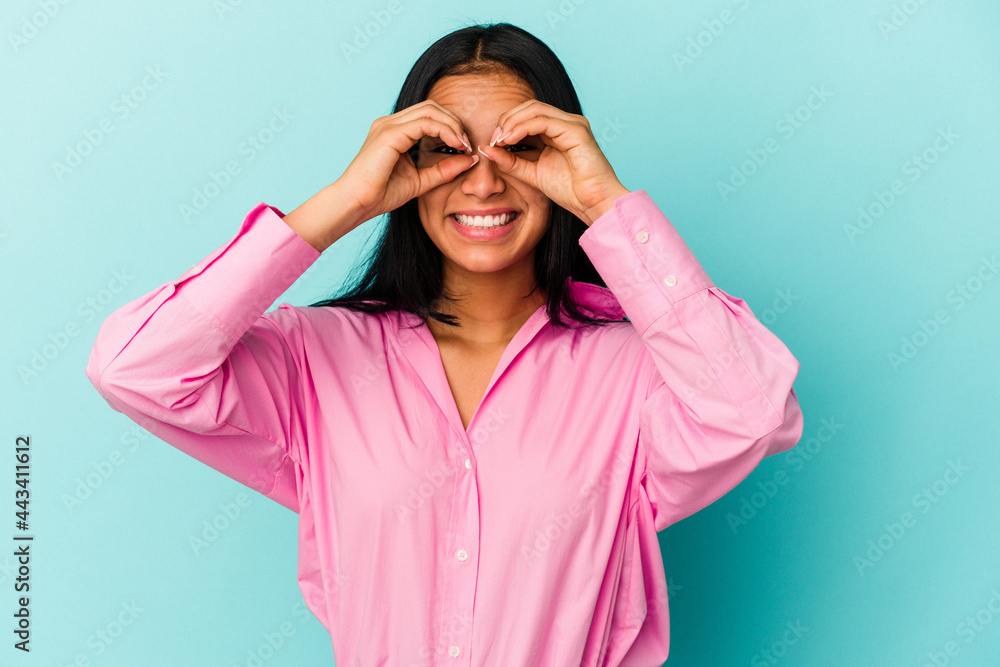 Young Venezuelan woman isolated on blue background showing okay sign over eyes Young Venezuelan woman isolated on blue background showing okay sign over eyes