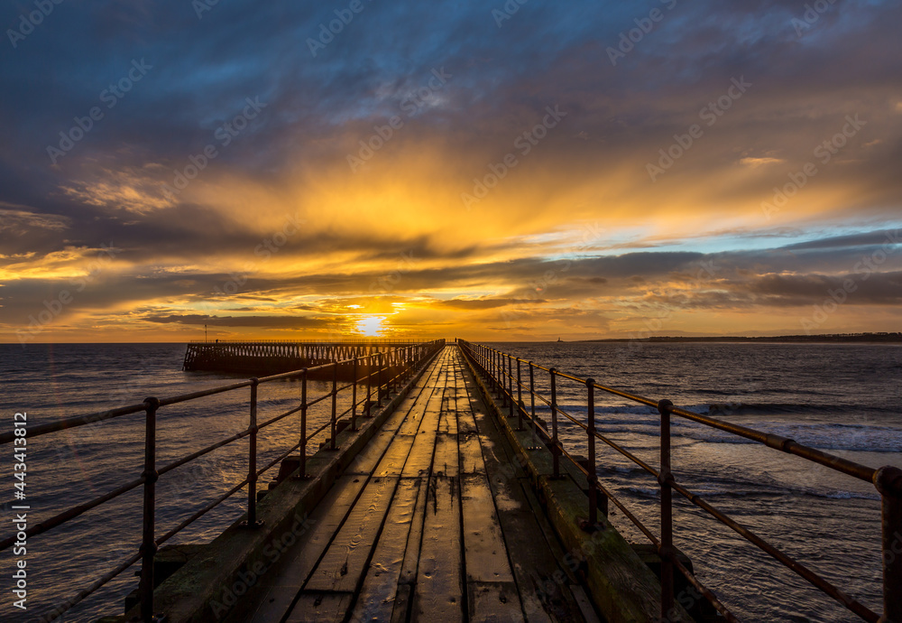 Obraz premium A glorious morning at Blyth beach, with a beautiful sunrise over the old wooden Pier stretching out to the North Sea