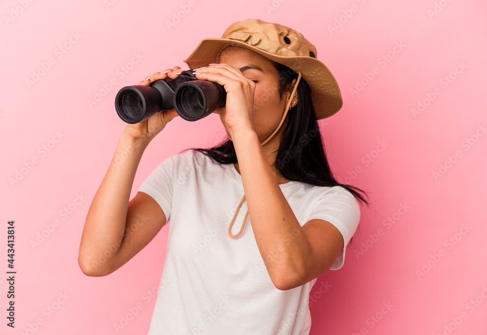 Young mixed race explorer woman holding binoculars isolated on pink background Young mixed race explorer woman holding binoculars isolated on pink background