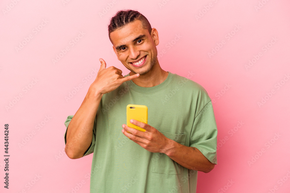 Young Venezuelan man holding a mobile phone isolated on pink background showing a mobile phone call gesture with fingers. Young Venezuelan man holding a mobile phone isolated on pink background showing a mobile phone call gesture with fingers.