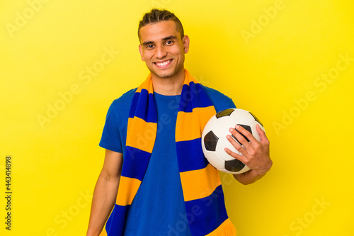 Young venezuelan man watching soccer isolated on yellow background happy, smiling and cheerful.