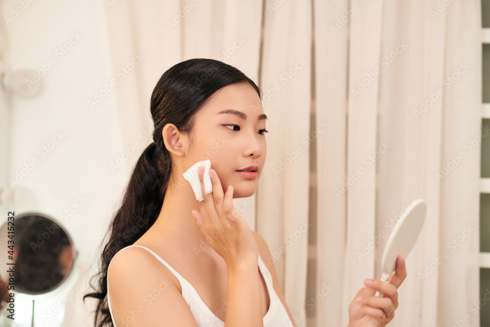 Young woman with cotton pad cleaning her face near mirror Young woman with cotton pad cleaning her face near mirror