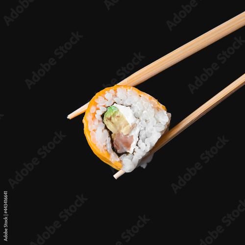 One piece of sushi in chopsticks, isolated on black background. Japanese cuisine concept, copy space banner.