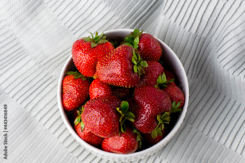 Juicy strawberries in a white plate. Fresh ripe delicious strawberries in a white bowl on a gray cloth background. Juicy strawberries in a white plate. Fresh ripe delicious strawberries in a white bowl on a gray cloth background.