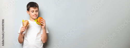 Happy small boy holding junk food: french fries and a burger. Fast food. Concept of unhealthy food.