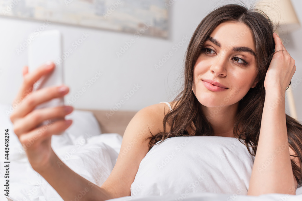 joyful young woman lying on bed and taking selfie on smartphone joyful young woman lying on bed and taking selfie on smartphone