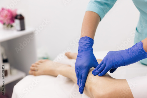 Physiotherapist worker woman assisting physical medical exercise recovery after injuries. Doctor in gloves examining painful knee of female patient leg trauma. Healthcare medical insurance concept