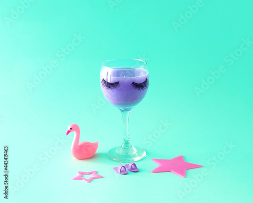 Glass cup with eyelashes and women's pink props. Celebration. Female party. Turquoise background.