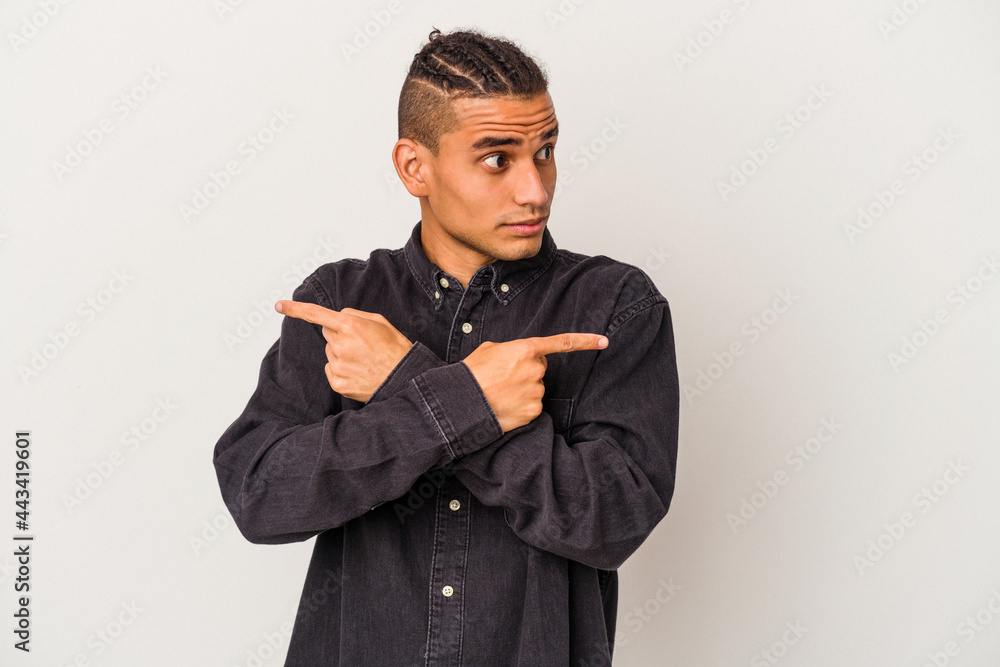 Young venezuelan man isolated on white background points sideways, is trying to choose between two options. Young venezuelan man isolated on white background points sideways, is trying to choose between two options.